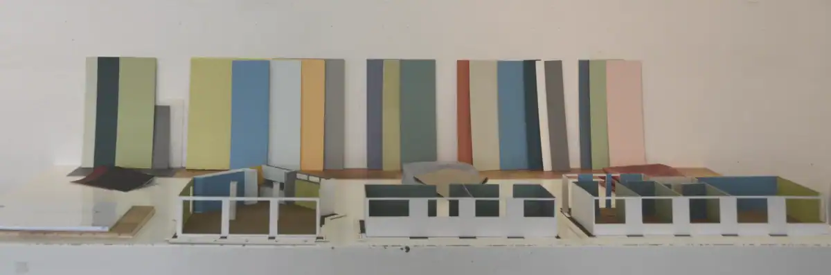 Schlafzimmer Gestaltung. Bemusterung mit Musterplatten in Originalfarbe und -material: Tapete mit floralem Muster in hellschimmerndem Grau vor tiefengrauem Hintergrund, Daneben Musterplatten der Wandfarben in tuchmattem, dunklem, rauchigem Blaugrau und hellem, warmen Muschelkal, sowie Farbakzent in Herbstgold. Leiste des dunkelbraunen Parketts.