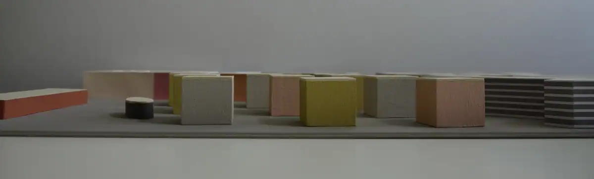 Schlafzimmer Gestaltung. Bemusterung mit Musterplatten in Originalfarbe und -material: Tapete mit floralem Muster in hellschimmerndem Grau vor tiefengrauem Hintergrund, Daneben Musterplatten der Wandfarben in tuchmattem, dunklem, rauchigem Blaugrau und hellem, warmen Muschelkal, sowie Farbakzent in Herbstgold. Leiste des dunkelbraunen Parketts.