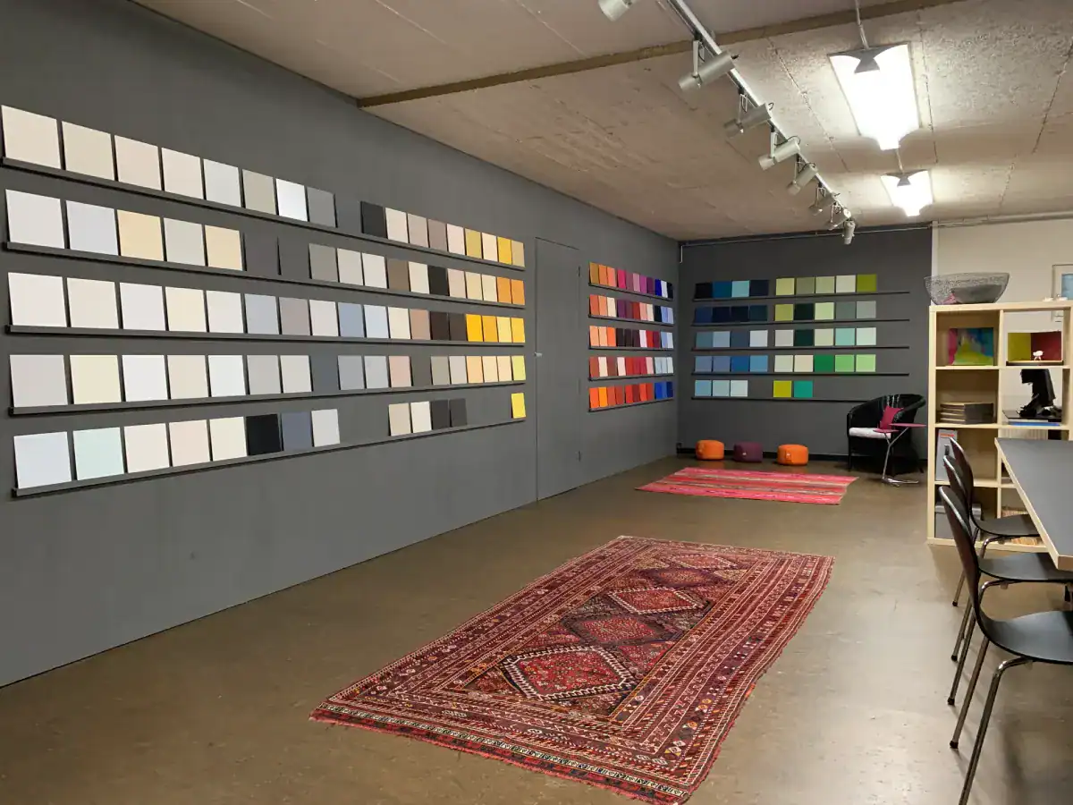 Atelier Farbgestaltung: UG-Raum mit Farbmusterwand. Farbige Muster auf Anthrazit-Wand, braun geölter Boden, Teppiche mit feinen rötlichen Ornamenten.