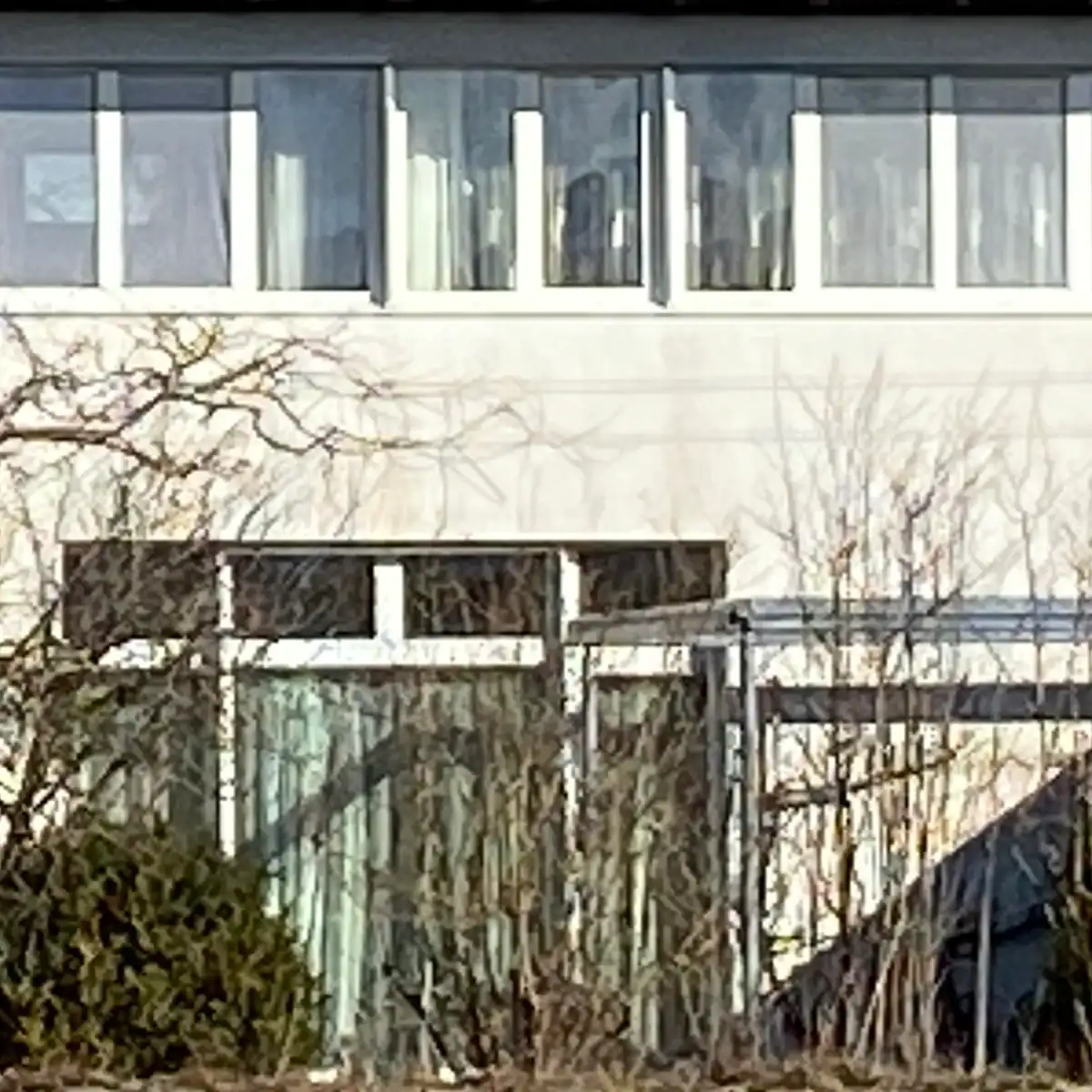 Ausschnitt einer modernen Hausfassade mit Fensterband im Obergeschoss und Fensterfront im Erdgeschoss sowie einermetallenen Pergola. Warmweisser Verputz und weisse Fenster.