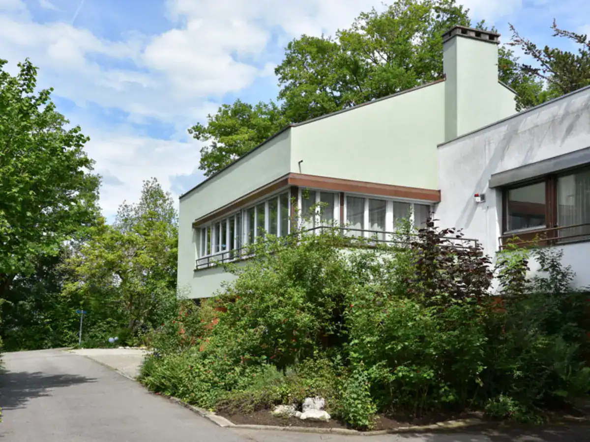 Blassgrüne Fassade eines Einfamilienhauess aus den 50er-Jahren in grüner Quartierumgebung.
