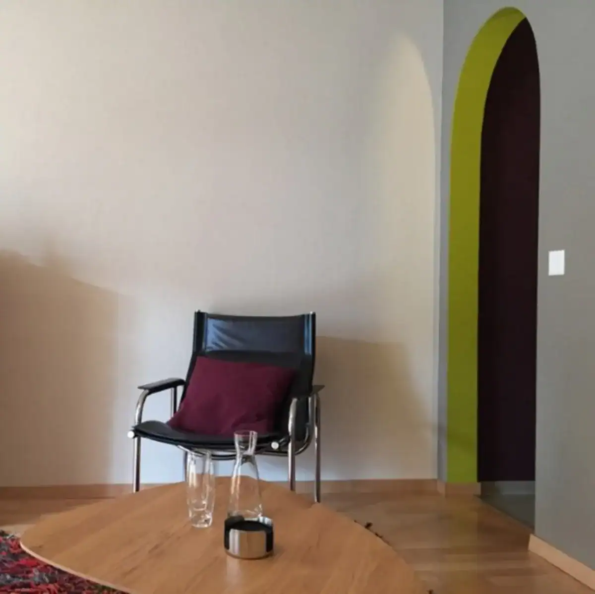 Farbgestaltung im Innenraum einer spirituellen Coaching-Praxis. Der Hauptraum mit warmen Weisstönen und mittlerer Umbranuance öffnet sich zu einem kleinen Nebenraum. Dieser ist in dunklem auberginefarbenem Violettton gehalten mit strahlendem Olivgrün an der Stirnseite des Durchgangs.