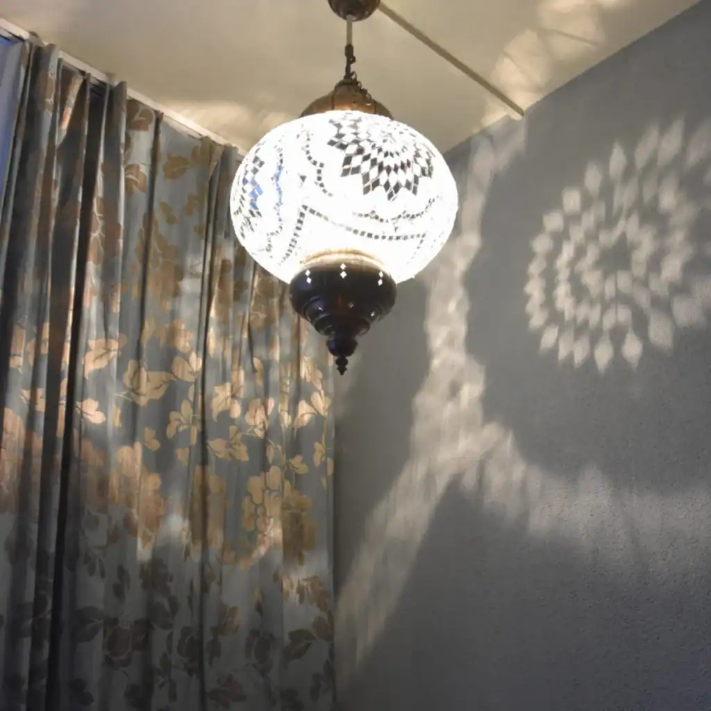 Inspirationsbild: Eine orientalische Hängeleuchte verzaubert Wand und Vorhang in ruhigem Graublau mit floralen Lichtornamenten in Silber.