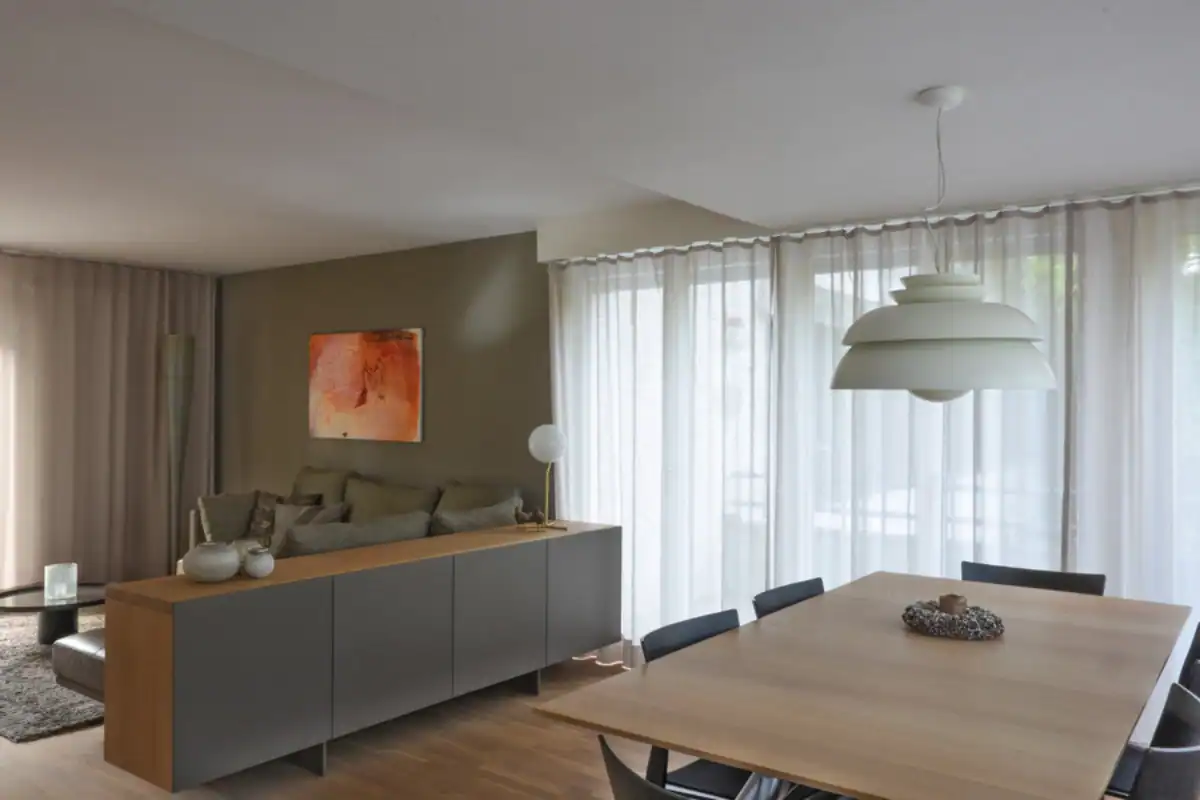 Farbgestaltung Wohnhaus: Eleganter Living- und Essbereich in Erdtönen mit Umbra-Mobiliar, schwarzen Holzstühlen und einem orangefarbenen Bild als Kontrast.