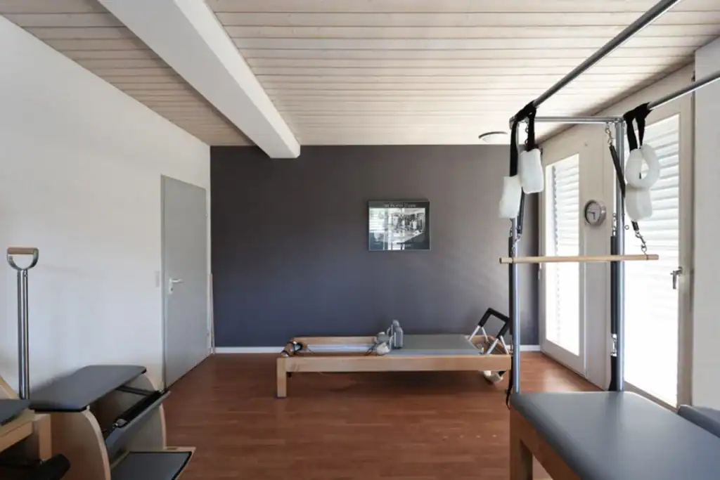 Farbgestaltung in einem Yoga- und Pilatesstudio – Blick in den Personal-Trainingsraum: Geräte in Holz und grauen Polsterflächen, Wände in Weiss mit Akzentwand in warmem Anthrazitton.