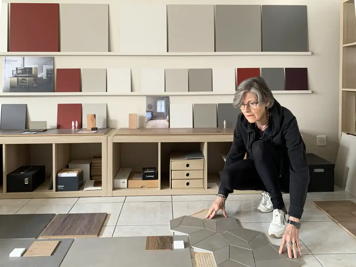 Regula Bielinski, Farbgestalterin, bereitet die Präsentation eines Farbkonzepts für ein Wohnhaus vor. Im Hintergrund an der Wand ist das Konzept mit verschiedenen Farb- und Materialmustern in Weiss-, Umbra- und Rottönen arrangiert. Am Boden sind weitere Musterplatten für den braunen Boden sowie umbrafarbene Steingutplatten für die Bäder ausgebreitet.
