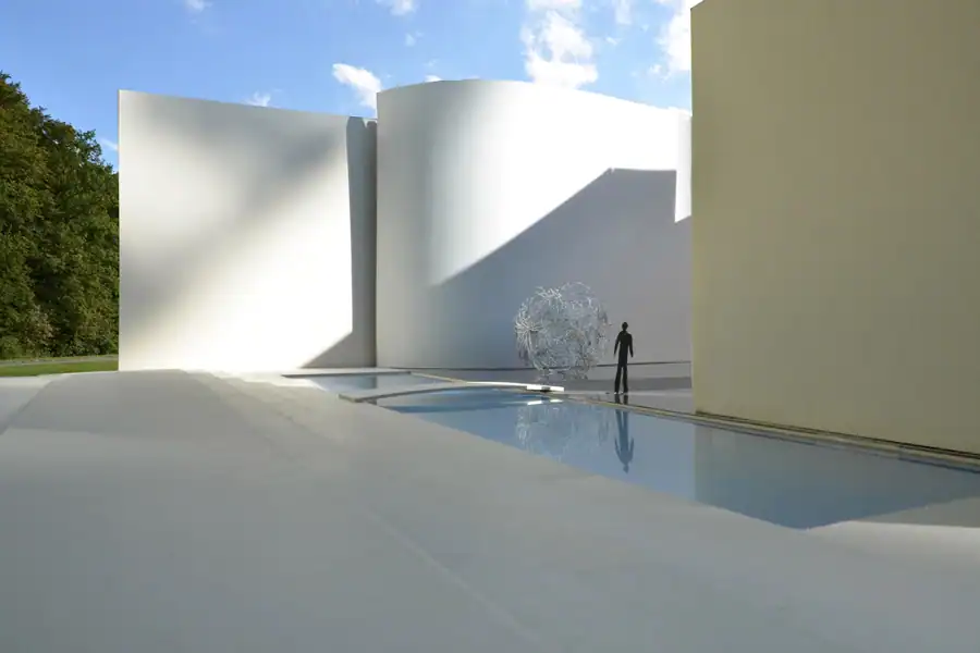 Modellfotografie, Studienprojekt Farbe & Licht: Aussenraum eines Museumsbaus. Weisse Bodenfläche mit Treppen zu einer blauen Wasserfläche, hohe, geschwungene Wände in Weiss und blassem Gelb. Silberfarbige Plastik und schwarze Figur vor stahlblauem Himmel. Starke Licht-Schatten-Kontraste, minimalistische und monumentale Wirkung.