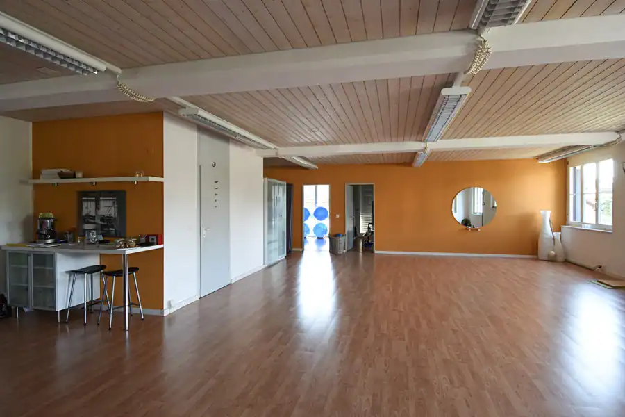 Farbgestaltung Studio für Yoga & Pilates, Steffisburg. Warmherziger Innenraum für Gruppen-Training. Schönes Tageslicht, Wände in Ocker und Weiss, brauner Parkettboden und helle Holzdecke.