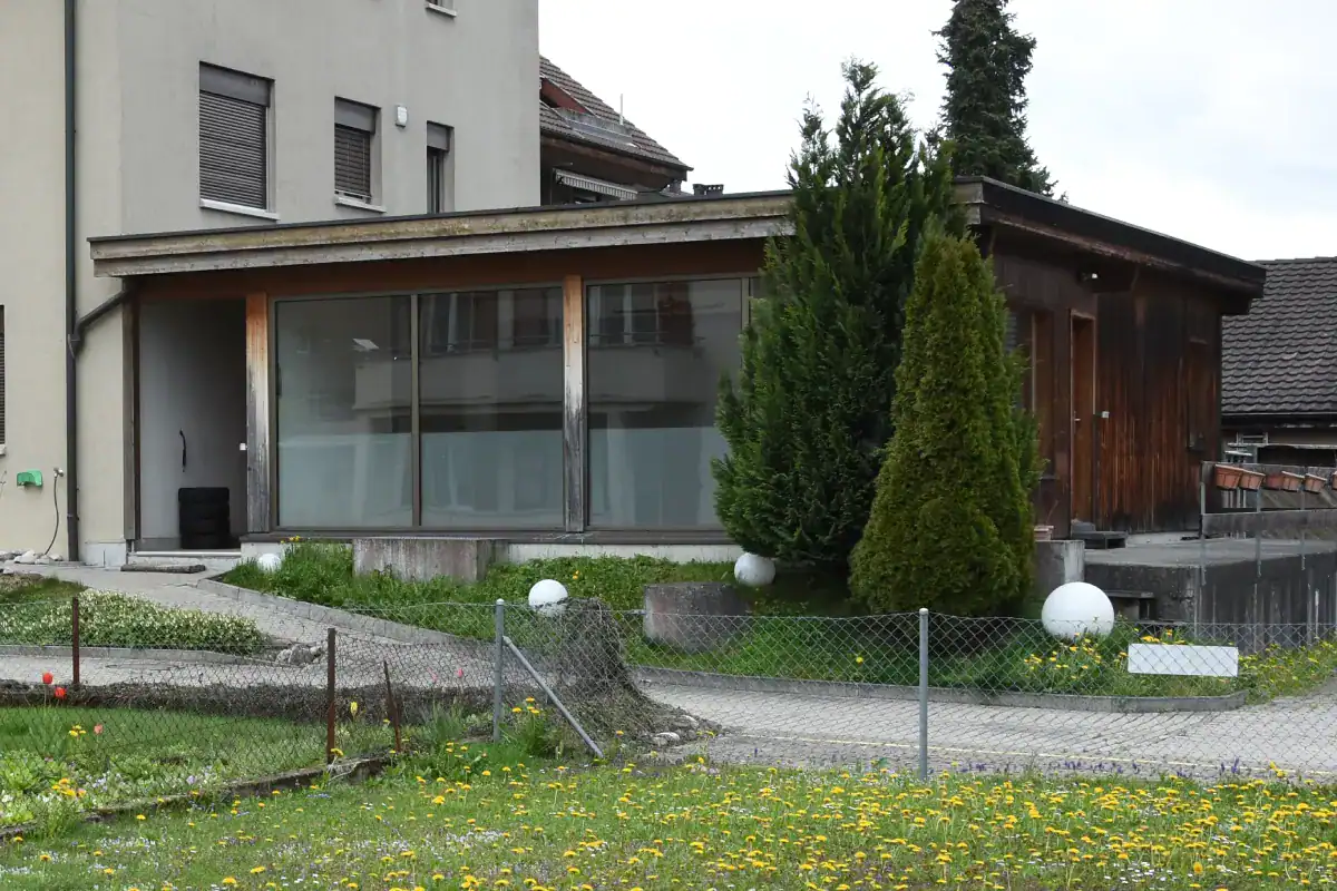 Küchenbereich und Gang mit Blick ins Schlafzimmer im Mittelgeschoss eines Einfamilienhauses aus den 50er-Jahren. Links die Küche mit hellen Fronten und anthrazitfarbenem Hochschrank, in der Mitte eine dekorative weisse Säule als Raumtrenner. Rechts der Durchgang zum Schlafzimmer mit blaugrüner Wand und die rote Akzentwand des Treppenhauses.