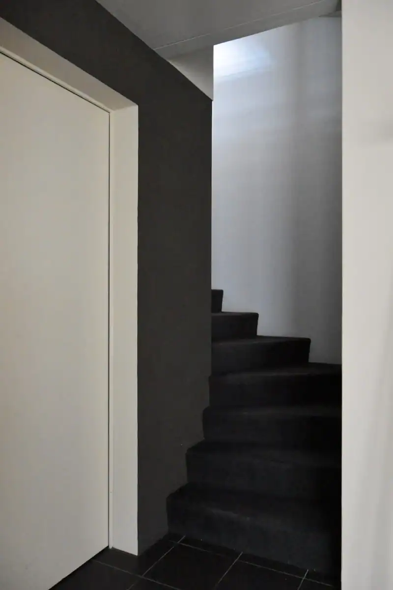 Studio für Yoga und Pilates. Personal-Trainingsraum. Blick von der Nordwand Richtung Akzentwand in Mauveanthrazit. Linke Wand zum Gruppentrainingsraum in Weiss, Tür hellgrau. Rechts Westwand in Weiss mit grossen Fenstern. Mitteldunkler honigfarbener Laminatboden und helle Holzdecke. Im Raum stehen verschiedene Pilates-Trainingsgeräte in hellem Holz und mit mittelgrauen gepolsterten Liege- und Sitzflächen. Die Anthrazitwand gibt dem Raum Halt und klare Orientierung.