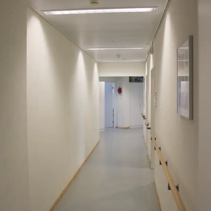 Treppenhaus im Mittelgeschoss des Einfamilienhauses aus den 50er-Jahren. Links Akzentwand in Rot, die vom Eingang bis ins Obergeschoss leitet, übrige Wände in abgetöntem Weiss. Treppentritte in hellbeigen Steinplatten, schwarze Metallbrüstung. An der rechten Wand ein längliches Holzregal auf mittlerer Höhe. Weiter oben ein schmaler, waagrechter Wanddurchbruch mit Sicht ins Wohnzimmer. Rechts schmaler Blick in den Livingbereich. Verschiedene Skulpturen und Dekorelemente.