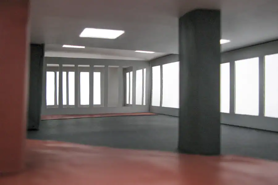 Treppenhaus im Mittelgeschoss des Einfamilienhauses aus den 50er-Jahren. Links Akzentwand in Rot, die vom Eingang bis ins Obergeschoss leitet, übrige Wände in abgetöntem Weiss. Treppentritte in hellbeigen Steinplatten, schwarze Metallbrüstung. An der rechten Wand ein längliches Holzregal auf mittlerer Höhe. Weiter oben ein schmaler, waagrechter Wanddurchbruch mit Sicht ins Wohnzimmer. Rechts schmaler Blick in den Livingbereich. Verschiedene Skulpturen und Dekorelemente.