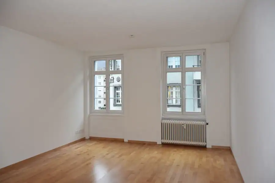 Studio für Yoga und Pilates. Personal-Trainingsraum. Blick von der Nordwand Richtung Akzentwand in Mauveanthrazit. Linke Wand zum Gruppentrainingsraum in Weiss, Tür hellgrau. Rechts Westwand in Weiss mit grossen Fenstern. Mitteldunkler honigfarbener Laminatboden und helle Holzdecke. Im Raum stehen verschiedene Pilates-Trainingsgeräte in hellem Holz und mit mittelgrauen gepolsterten Liege- und Sitzflächen. Die Anthrazitwand gibt dem Raum Halt und klare Orientierung.