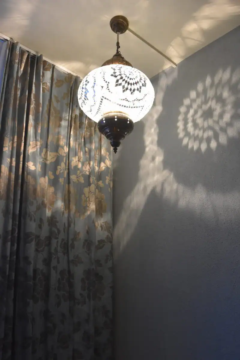 Schlafzimmer Gestaltung. Blick zur Nordostecke mit der Nische. Rechts ist ein Teil des hochwertigen dichten Vorhanges mit Silber-Bronze-Ornamenten. Links die helle Muschelkalkwand mit einer grossen hochformatigen Nische in Herbstgold, deren Boden im selben dunkelnbrauen Holz wie der Parkettboden beschaffen ist.